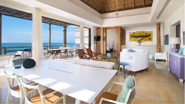 Una habitación amplia con un gran comedor, sofás blancos y vista al océano.