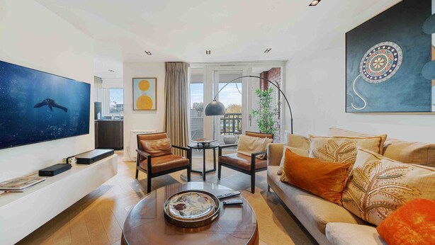 A modern living room with a large flat-screen TV, leather sofas, a coffee table, and a view of the city through large windows.