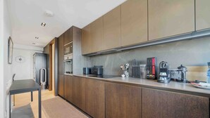 A modern kitchen with dark wooden cabinets, a stainless steel countertop, and various appliances including a coffee maker and a kettle.