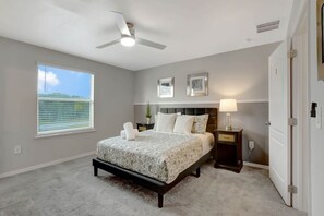 A bedroom with a bed, a nightstand, a ceiling fan, a window with blinds, and a door.