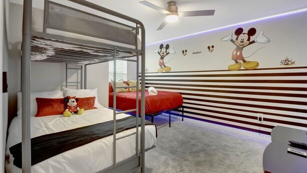 Ein Schlafzimmer mit Etagenbetten, Deckenventilator und einer Wand mit Comicfiguren-Aufklebern.