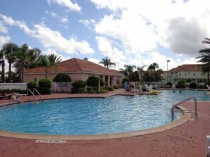 A swimming pool with a tiled deck, surrounded by palm trees and a building with a red roof. - Amazing Deal 3/2 Close to Disney Resort Pool (Kissimmee)