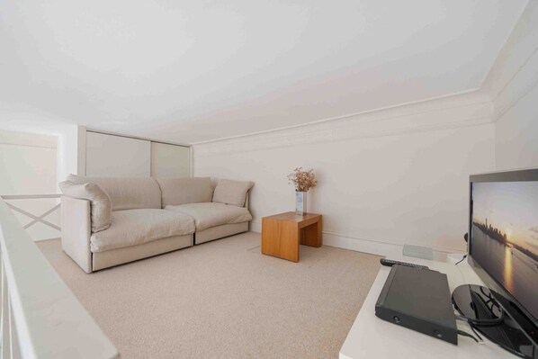 A minimalist living room with a sofa, a small wooden side table, a television, and a remote control.