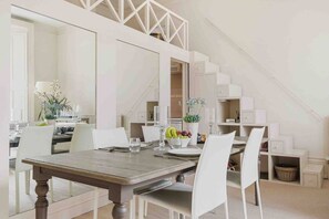 A dining area with a wooden table, white chairs, and a large mirror above.