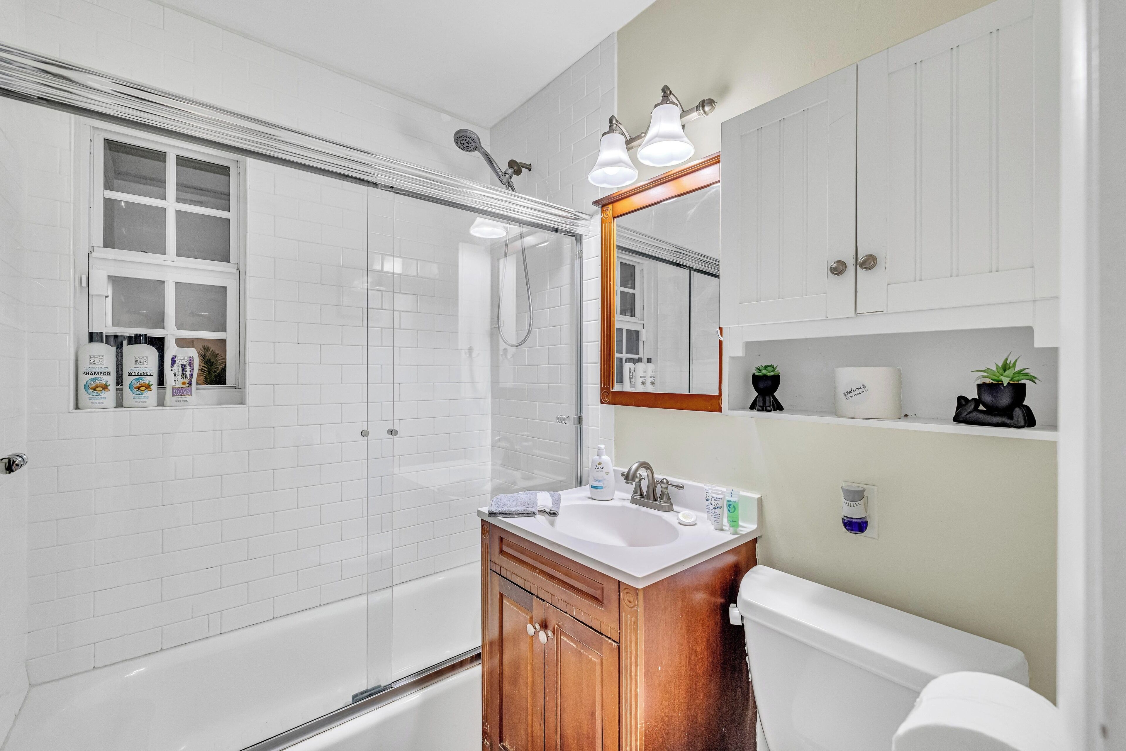 A modern bathroom with a glass-enclosed shower, a wooden vanity, a white sink, and a toilet.