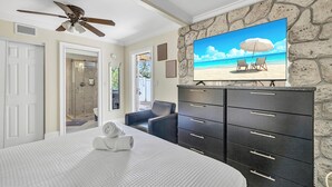 Una camera da letto con un letto grande, una televisione che mostra una spiaggia e un muro in pietra, oltre a una ventola a soffitto.