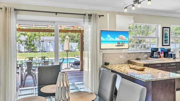 Una cucina moderna con una grande isola, una zona pranzo con tavolo in vetro e vista su piscina e spiaggia attraverso ampie finestre.