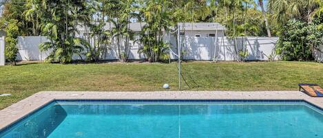 A rectangular swimming pool with a tiled edge, surrounded by a brick patio with lounge chairs and towels.