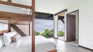 Un dormitorio con una cama de madera, vistas a zonas verdes y una puerta que da a otra habitación.