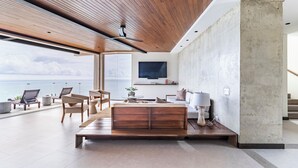 Una sala de estar moderna con techo de madera, un televisor grande y vista al mar.