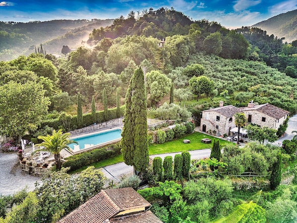 Une villa avec piscine, entourée d’une végétation luxuriante et de collines.
