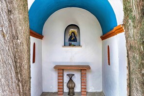 Une alcôve en arc surmontée d’une icône religieuse, avec une petite table et un vase.