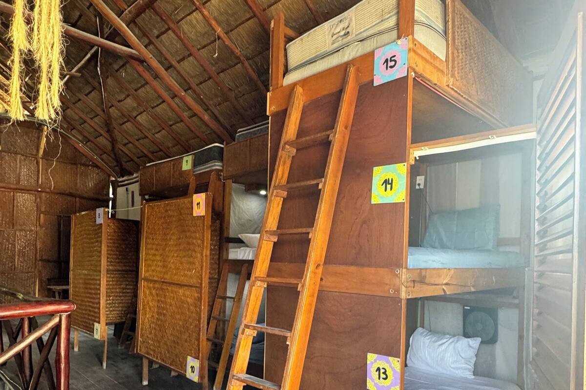 A rustic cabin with wooden bunk beds, numbered tags, and a ladder.