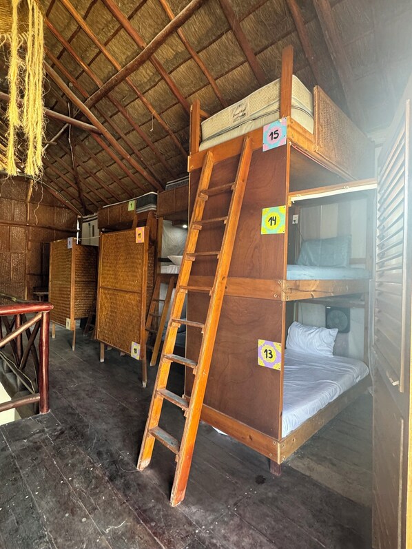 A rustic cabin with wooden bunk beds, numbered tags, and a ladder.