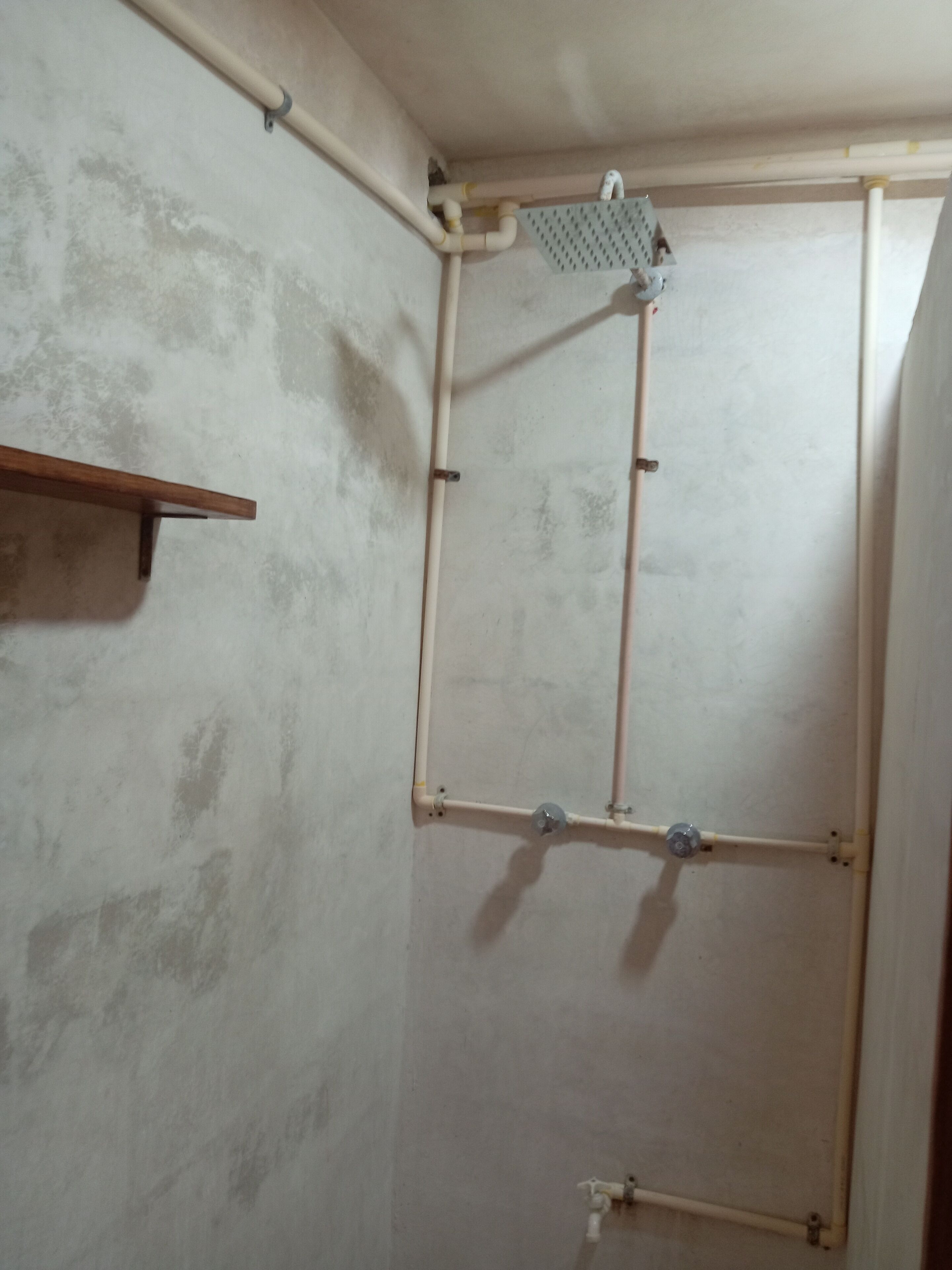 Une pièce avec un espace douche, une étagère en bois et un mur en béton.