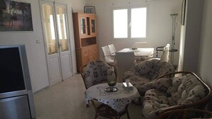 A living room with a sofa, a round table with a lace tablecloth, a cabinet, and a TV.