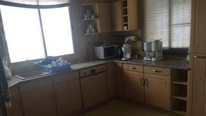 A kitchen with wooden cabinets, a microwave, a coffee maker, and a window with blinds.