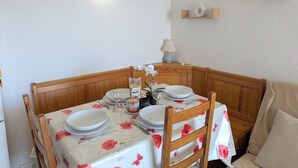 A dining area with a table set for four, wooden chairs, a wall-mounted light, and small shelves with decorative items. - Sol-y-Days Sloop, two bedrooms with views of the Salins (Le Grau-du-Roi)