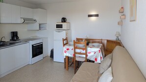 A compact kitchen with a stove, microwave, and coffee maker. There is a dining table with chairs and a sofa in the living area. - Sol-y-Days Sloop, two bedrooms with views of the Salins (Le Grau-du-Roi)