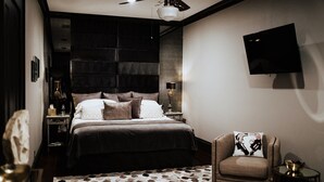 Un dormitorio moderno con una cama grande, una silla, un televisor y un ventilador de techo.