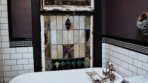 Un baño con una bañera independiente, una lámpara de araña de cristal colgante y un espejo con un marco decorativo.