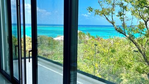 Un intérieur moderne doté de grandes baies vitrées qui offrent une vue sur un océan turquoise et un paysage côtier.