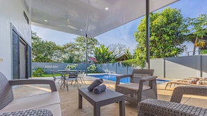 Un patio exterior con mobiliario de mimbre, una piscina y vistas al entorno cubierto de vegetación.