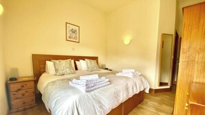 A bedroom with a wooden bed, white bedding, a bedside table with a lamp, and a framed picture on the wall. - Llaethdy Rachel, Lampeter (Aberaeron)