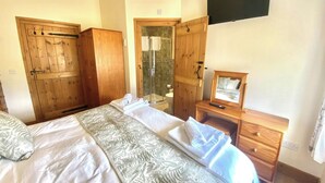 A bedroom with a bed, wooden wardrobe, a shower area, and a television mounted on the wall. - Llaethdy Rachel, Lampeter (Aberaeron)