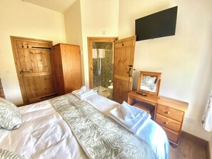 A bedroom with a bed, wooden wardrobe, a shower area, and a television mounted on the wall. - Llaethdy Rachel, Lampeter (Aberaeron)