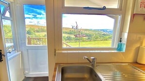 A kitchen with a stainless steel sink, a window with a view of a landscape, and a door leading to an outdoor area. - Llaethdy Rachel, Lampeter (Aberaeron)