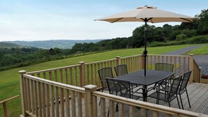 A deck with a table and chairs, an umbrella, and a view of the countryside. - Llaethdy Rachel, Lampeter (Aberaeron)