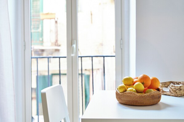 A balcony with a wicker basket containing lemons and oranges, a white chair, and a view of buildings through the glass doors. - Cara Palermo (Palermo)