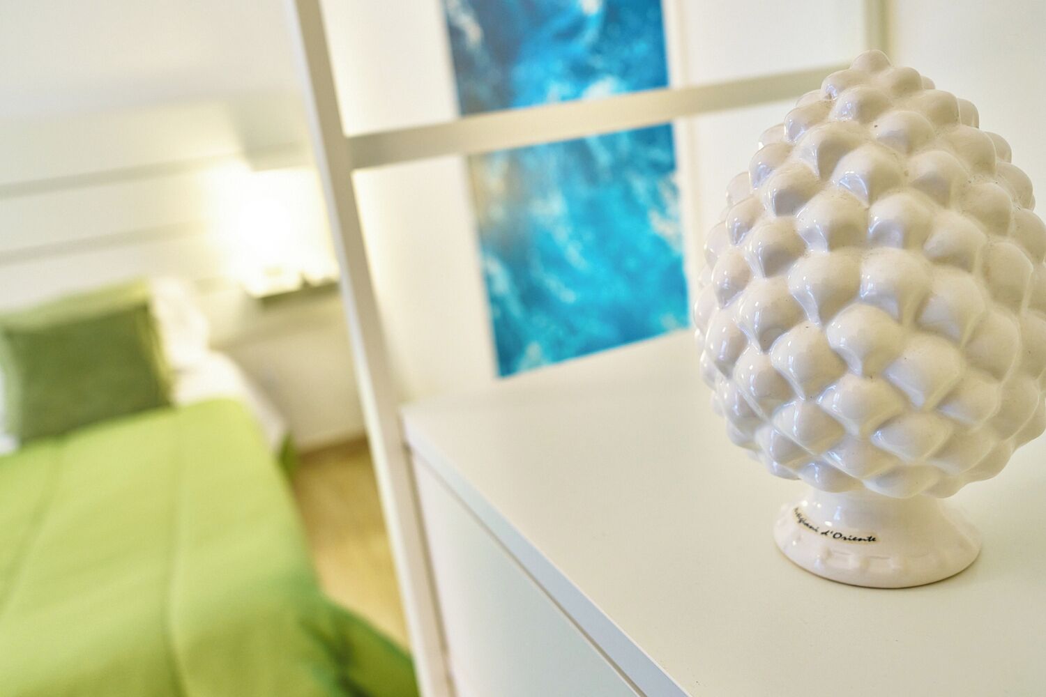 A white spherical object on a white surface, a green bedspread, and a blue painting in the background.