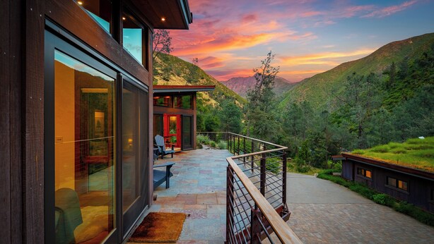 Uma casa moderna com fachada de vidro, varanda e vista para uma paisagem montanhosa.