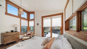Um quarto espaçoso com uma cama grande, cabeceira de madeira e vista para um jardim por uma porta deslizante.