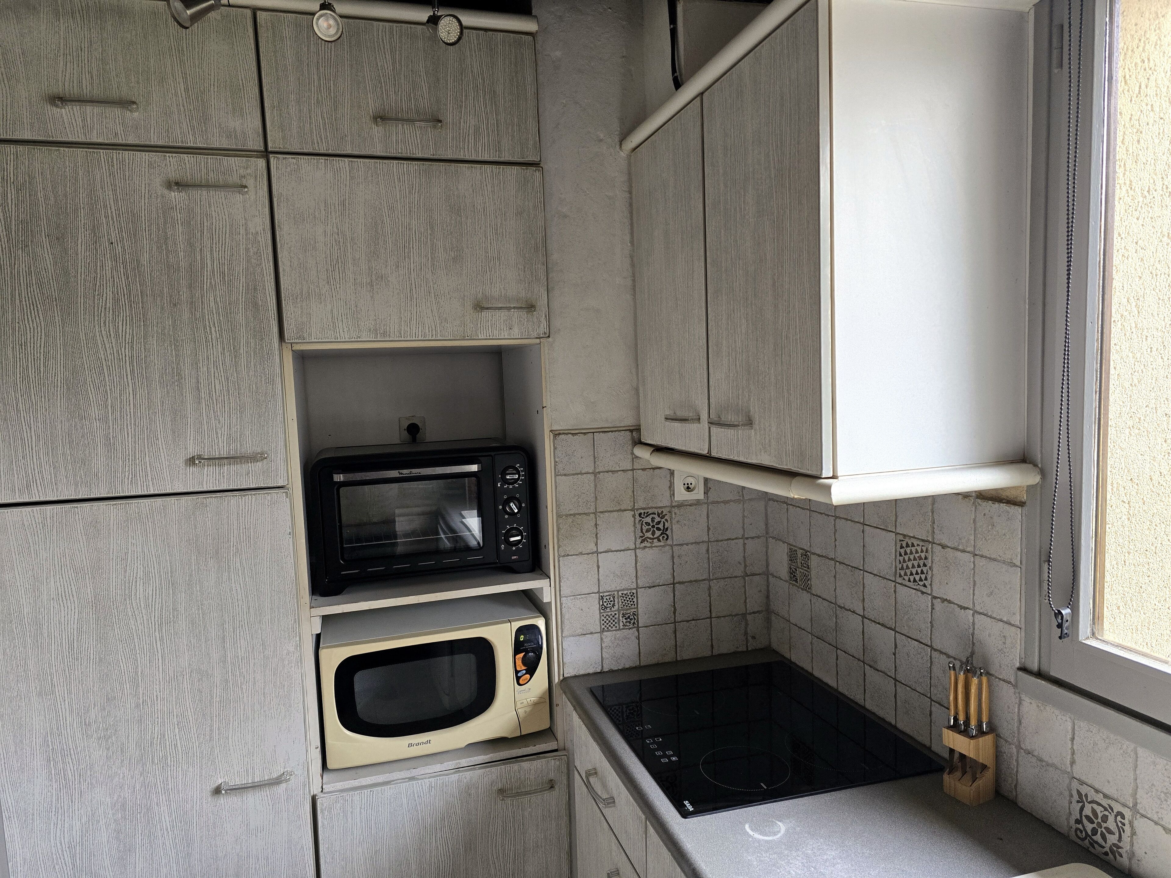 A compact kitchen with a built-in microwave, oven, and induction cooktop, featuring grey cabinetry and tiled backsplash.
