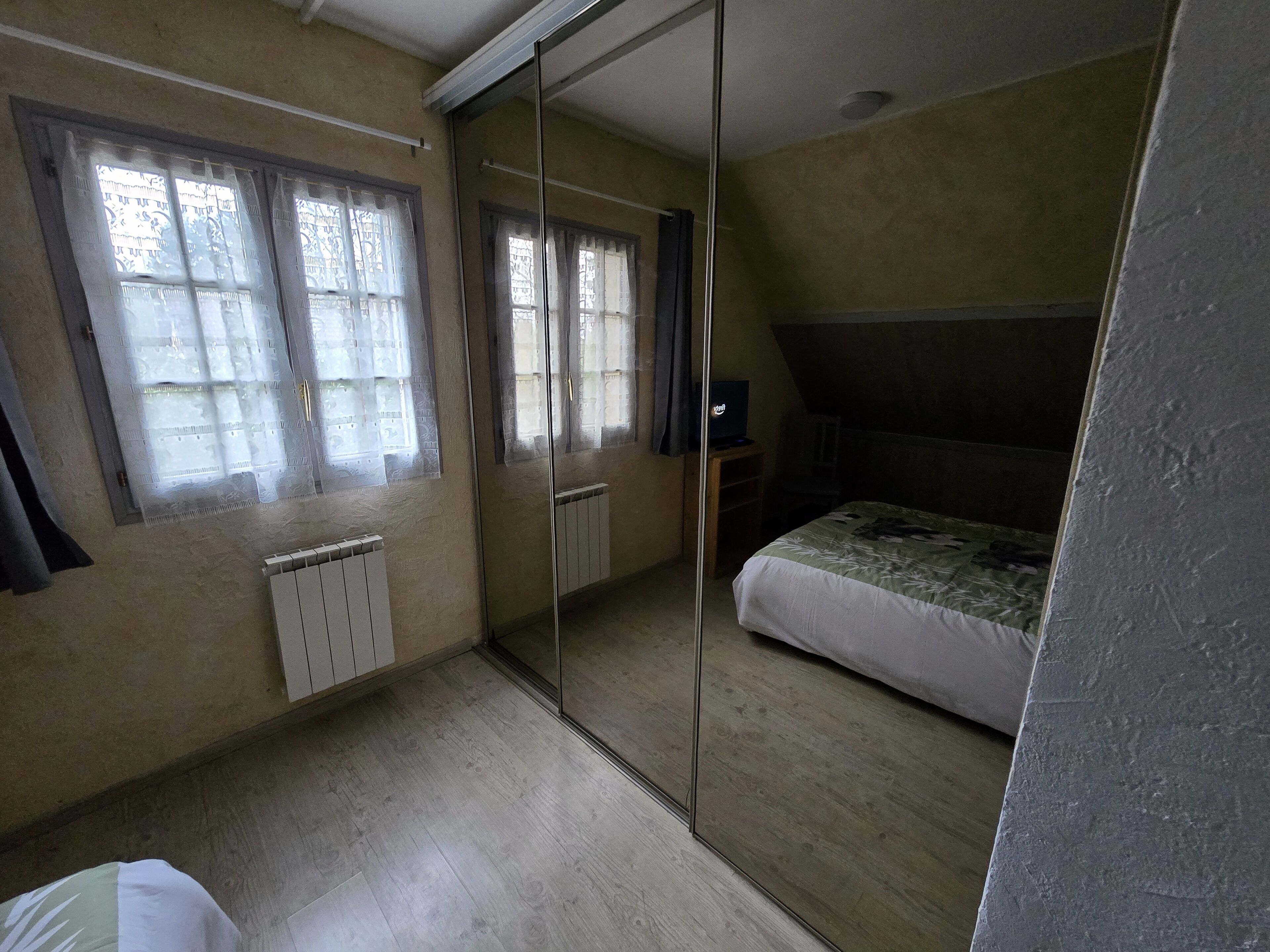 Een slaapkamer met een bed, een radiator, een raam met gordijnen en een spiegel.