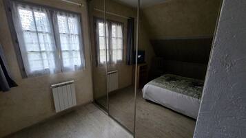 Een slaapkamer met een bed, een radiator, een raam met gordijnen en een spiegel.
