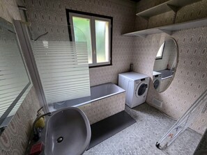 Une petite salle de bain comprenant un lavabo, un lave-linge, un miroir et une fenêtre.