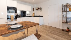 A modern kitchen with white cabinetry, a wooden dining table, and a built-in oven. - Stylish Flat Near Charlton Station - Pass the Keys (London)