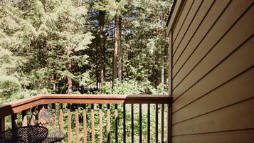 A wooden deck with a metal table and chair, overlooking a dense forest.
