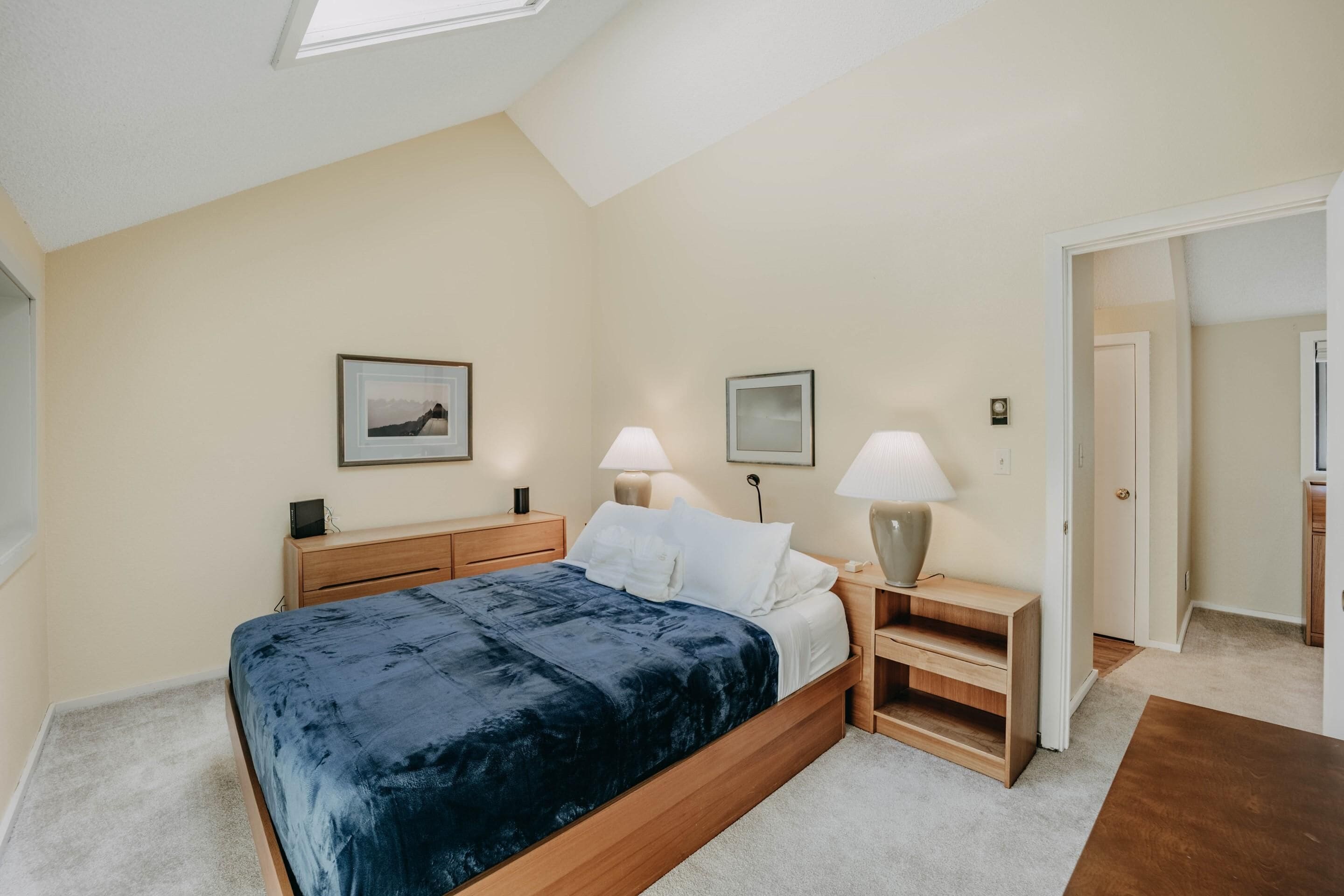 Een slaapkamer met een bed, nachtkastjes, lampen en ingekaderde foto’s aan de muur.
