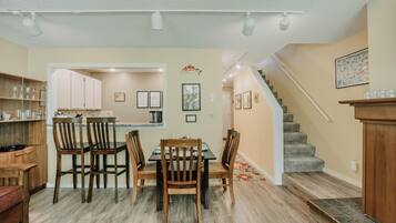 A dining area with a wooden table and chairs, a kitchen with cabinets, and a staircase leading upstairs.