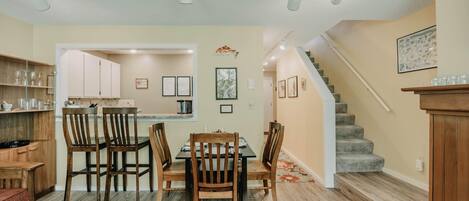 A dining area with a wooden table and chairs, a kitchen with cabinets, and a staircase leading upstairs.