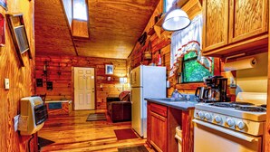 A wooden cabin interior with a kitchen area featuring a stove, refrigerator, and wooden cabinets. - Indian Creek Cabin at Ponderosa (Cherokee)