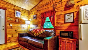 A cozy cabin interior with a leather sofa, a small wooden cabinet, a microwave, and a refrigerator. - Indian Creek Cabin at Ponderosa (Cherokee)