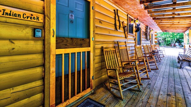 A wooden cabin with a porch, rocking chairs, and a blue door with a 'No Smoking' sign. - Indian Creek Cabin at Ponderosa (Cherokee)