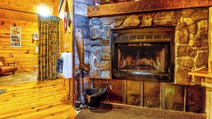 A cozy room with a stone fireplace, wooden walls, and a comfortable seating area. - Indian Creek Cabin at Ponderosa (Cherokee)