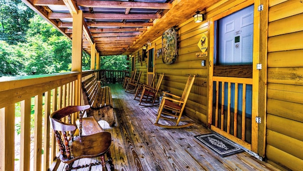 Une cabane en bois dotée d’une véranda, de fauteuils à bascule et d’une porte avec une fenêtre.